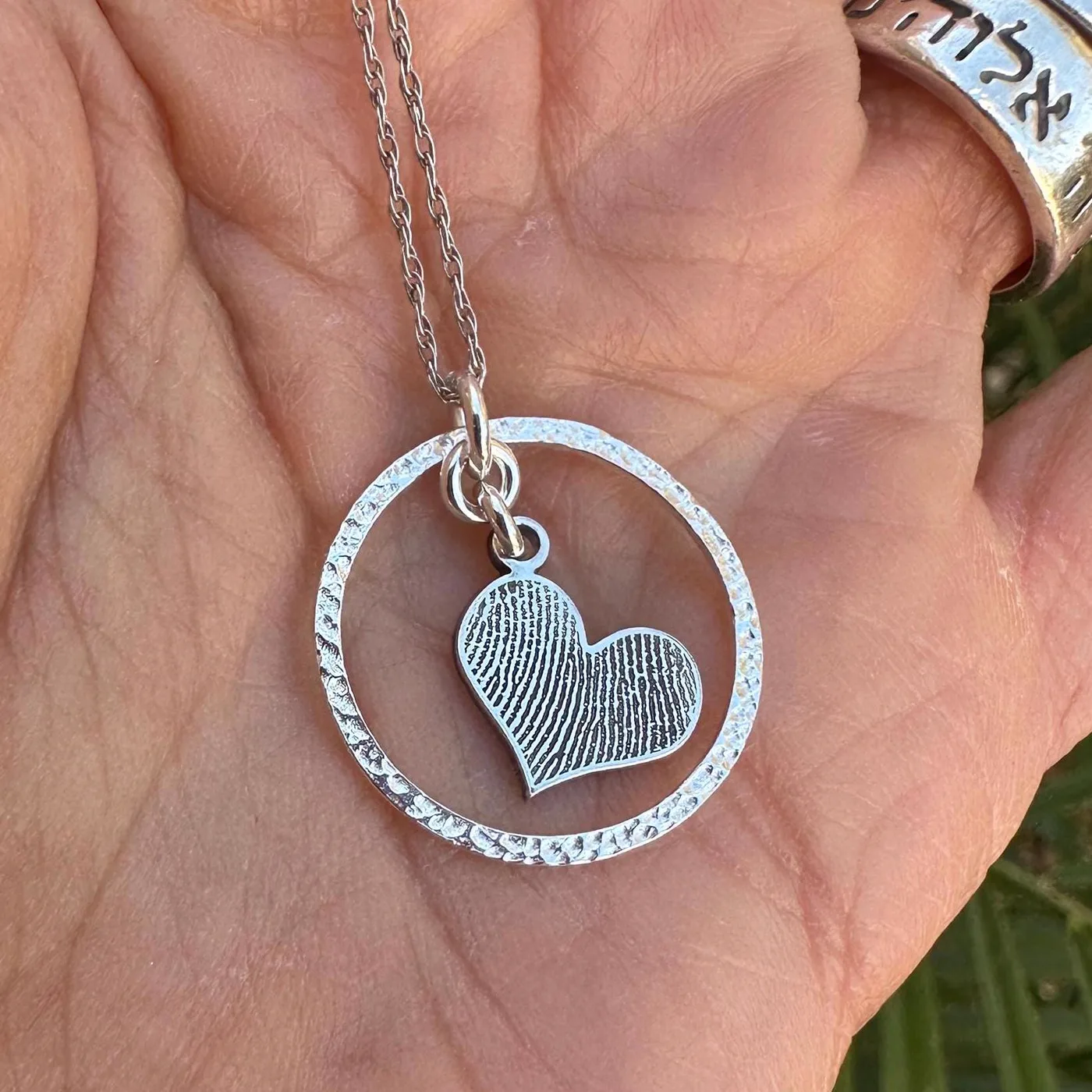 A small fingerprint heart held inside a hammered silver circle, on charred wood