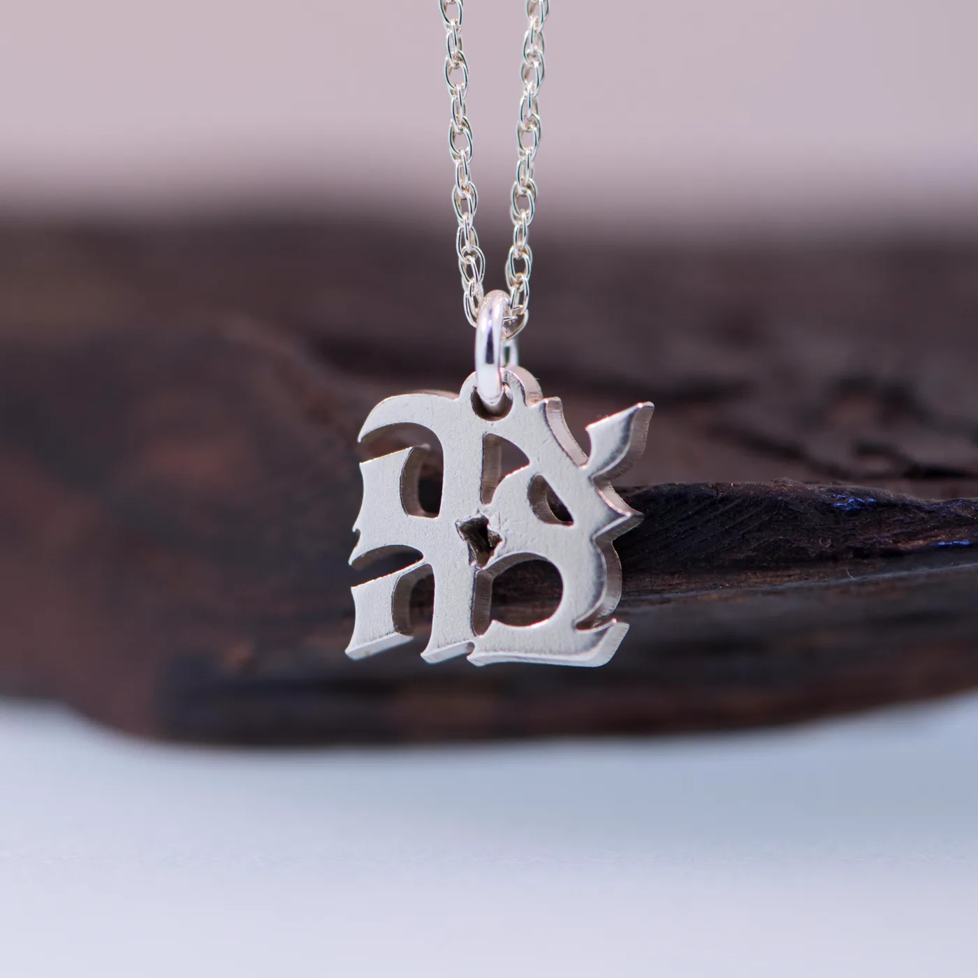 AHAVA charm in sterling silver, the Hebrew letters set in a square, on charred wood