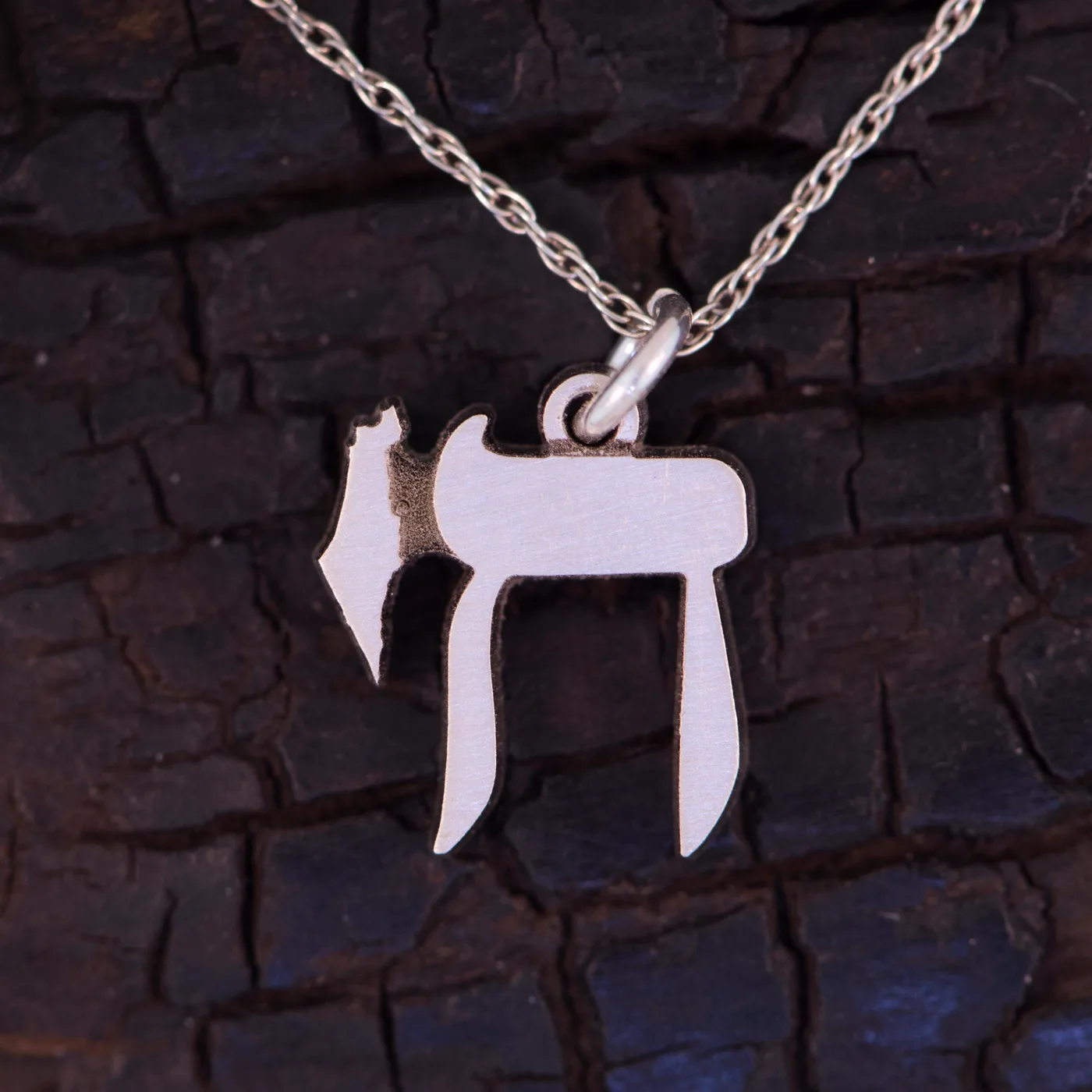 Solid Chai charm in silver on a fine chain, on charred wood