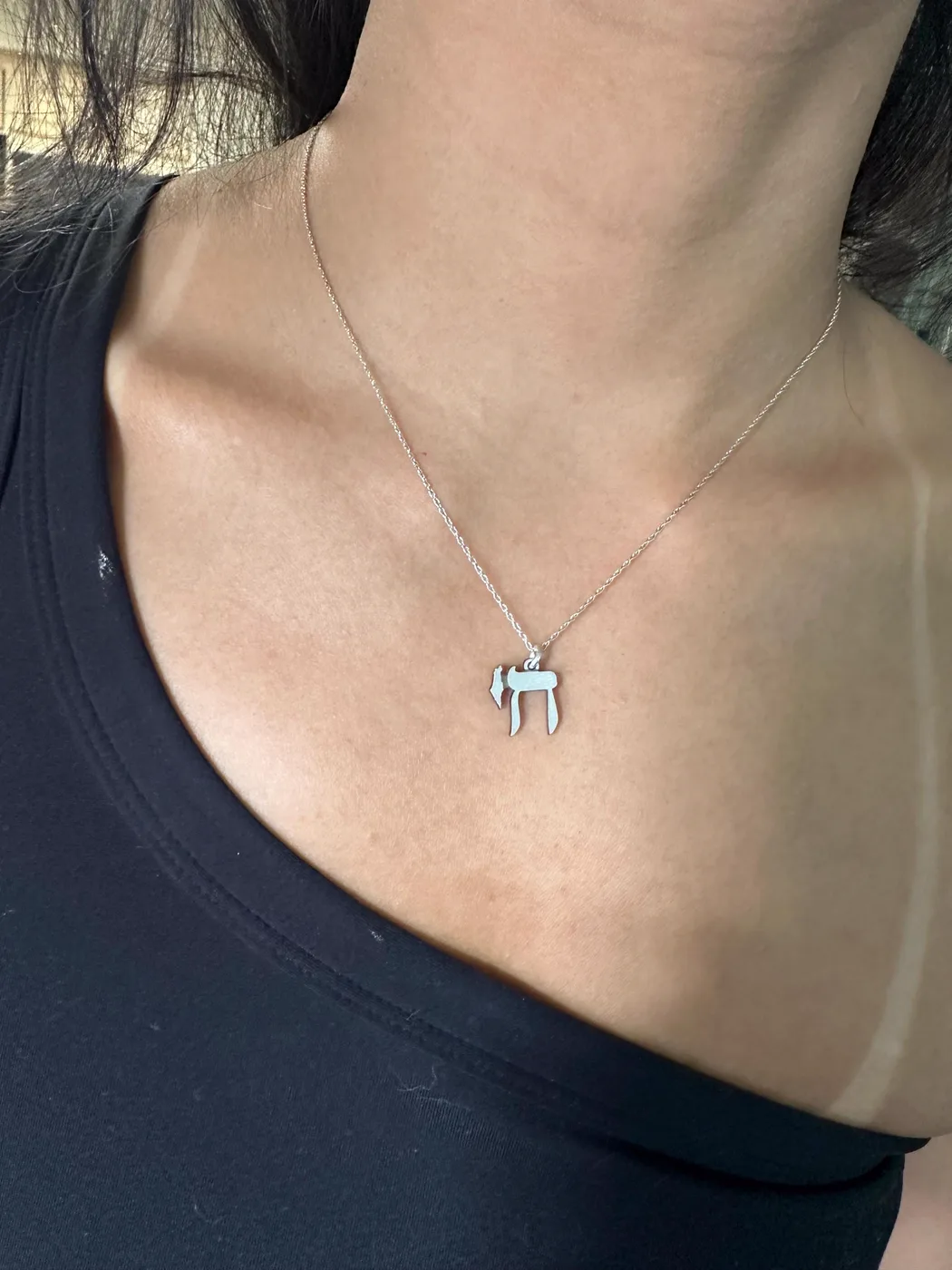 The Chai charm worn at the collarbone over a black top