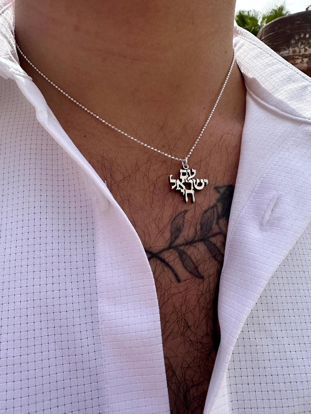 The pendant worn on a ball chain over an open white shirt