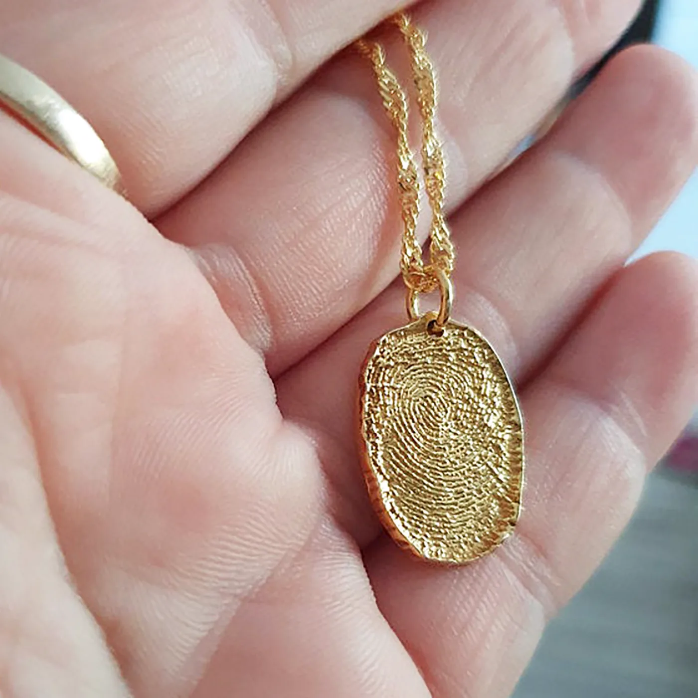 A gold fingerprint charm held in a hand, showing its true size