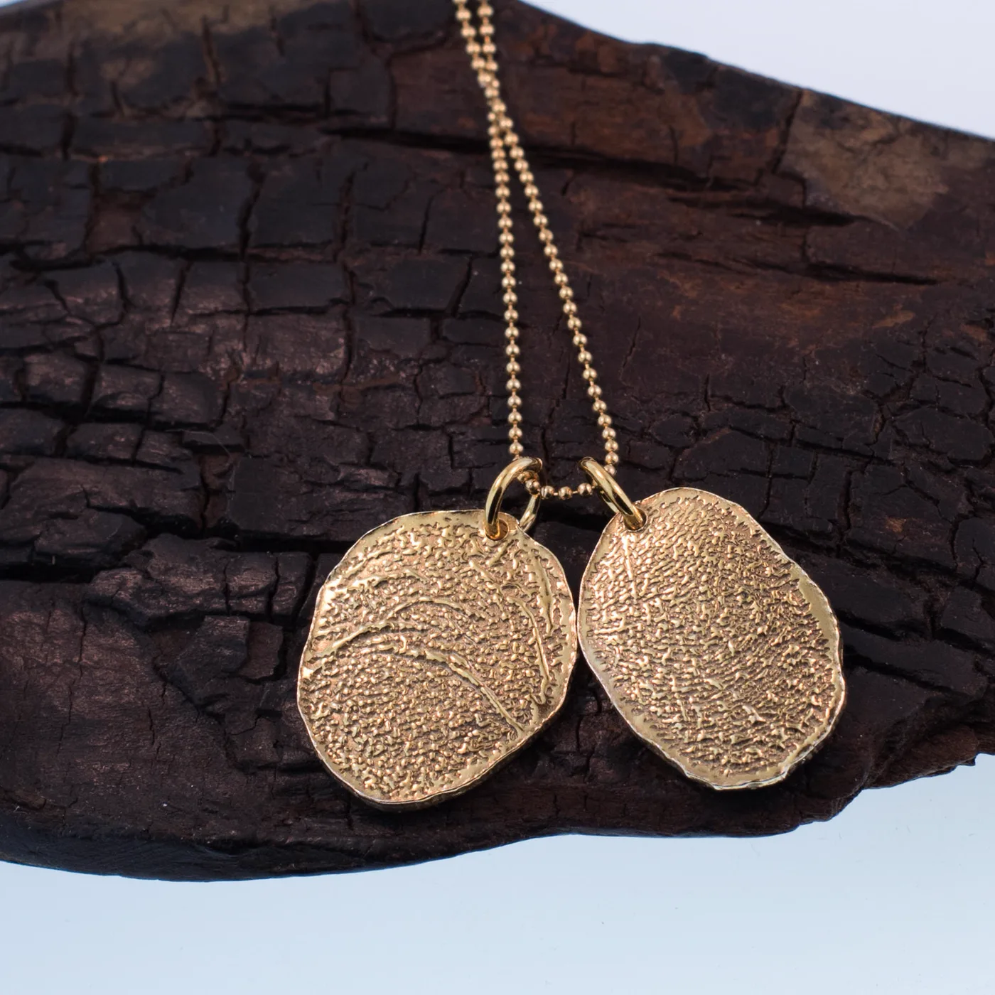 Two gold fingerprint charms hanging together on charred wood