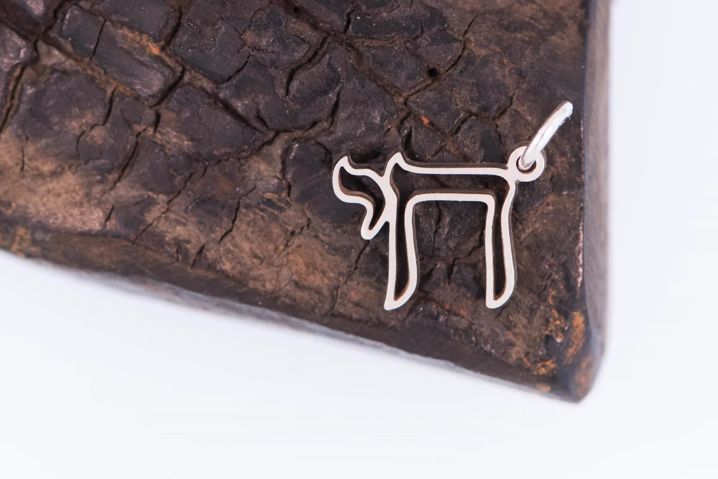 Hollow outline Chai charm in sterling silver, on charred wood