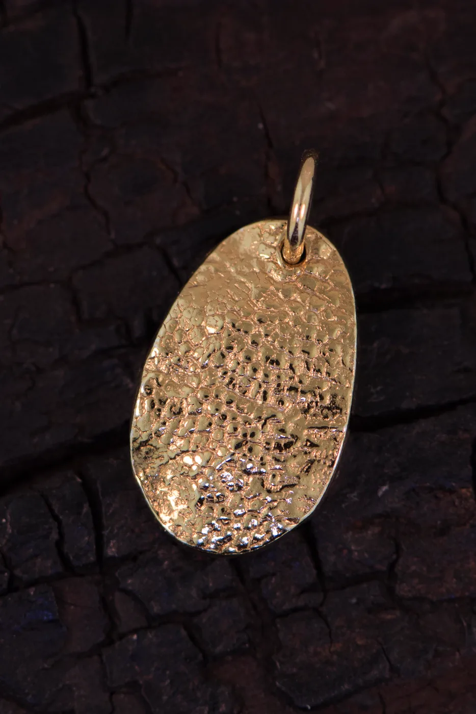 A gold teardrop charm carrying a pet's nose print, on charred wood
