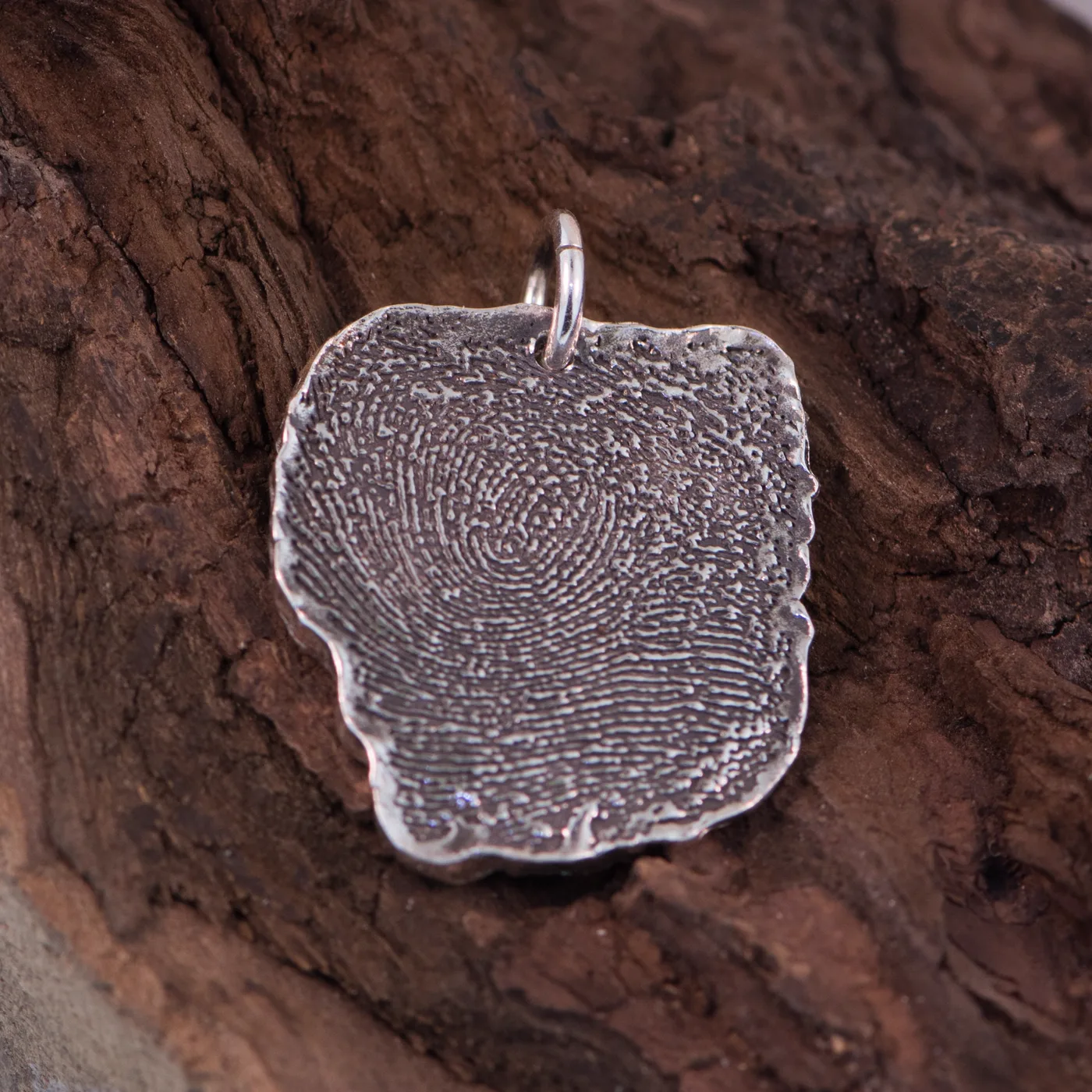 Silver fingerprint charm, the ridges of a real print pressed into the metal, on charred wood
